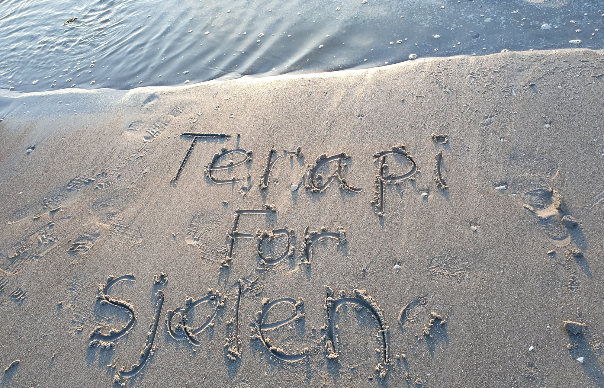 Teksten 'Terapi for sjælen' skrevet i blødt strandsand
